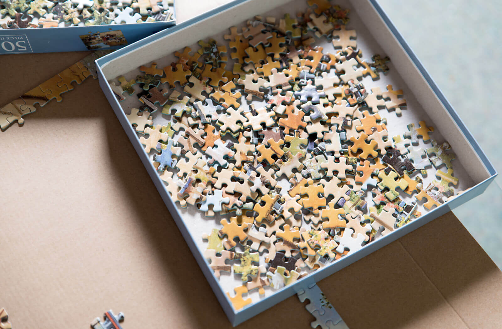 An open box of puzzle pieces sitting on a piece of cardboard with the start of a puzzle on it.