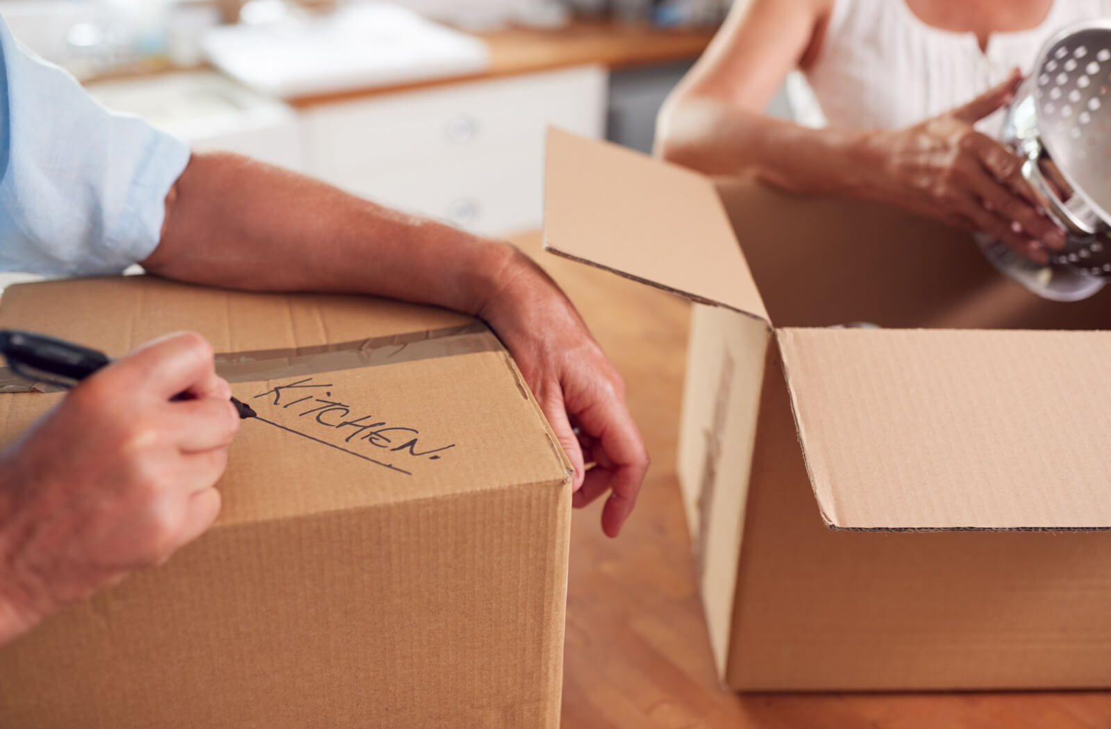 A close-up of an older adult writing the word "Kitchen" on a box while downsizing to prepare to move to assisted living.