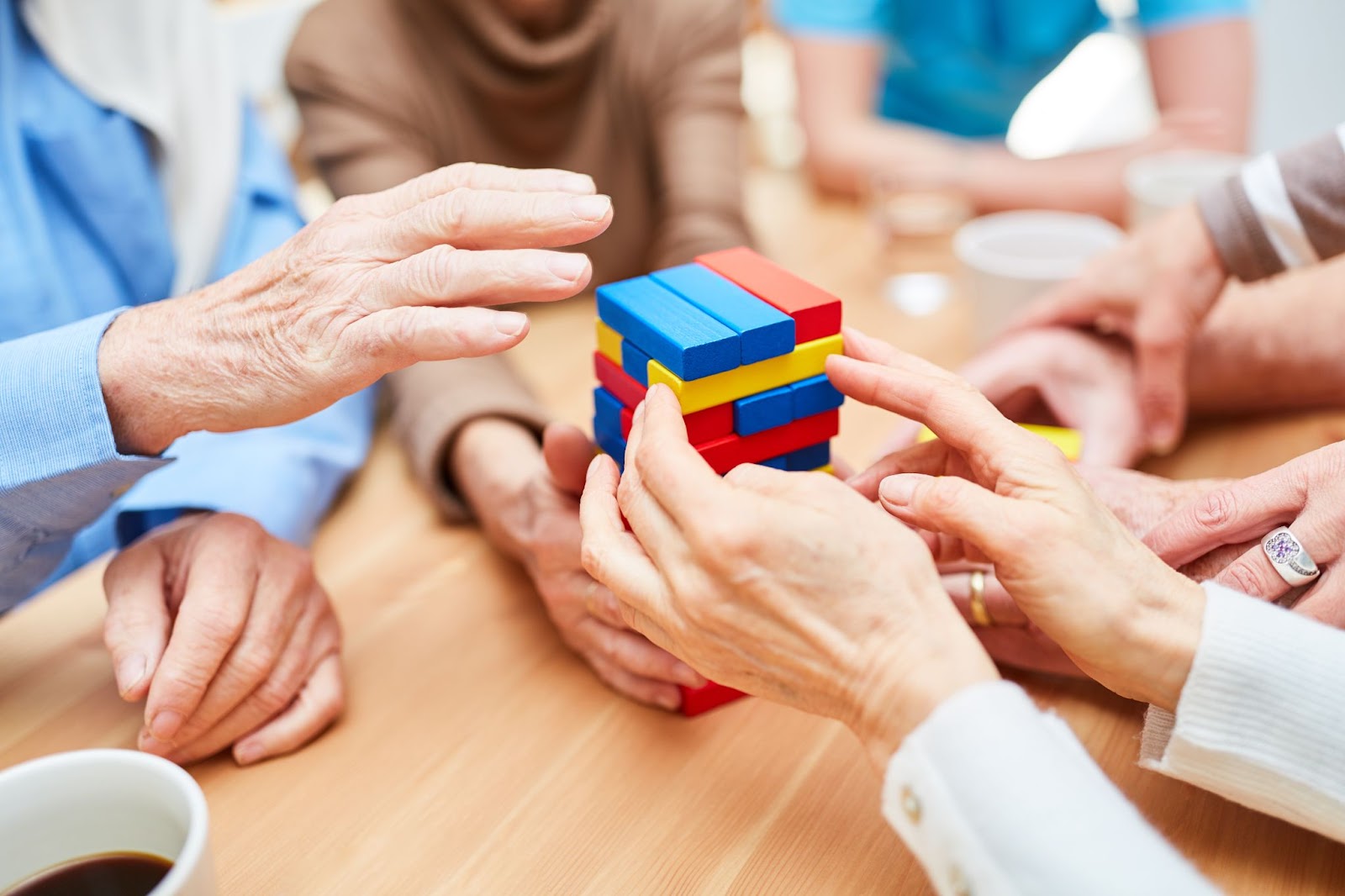 A close-up of hands from a group of seniors with dementia, playing a game of Jenga using colorful pieces.