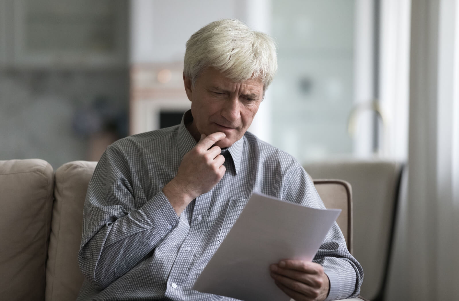 An older adult with dementia sitting on the couch and staring at a legal document in confusion.