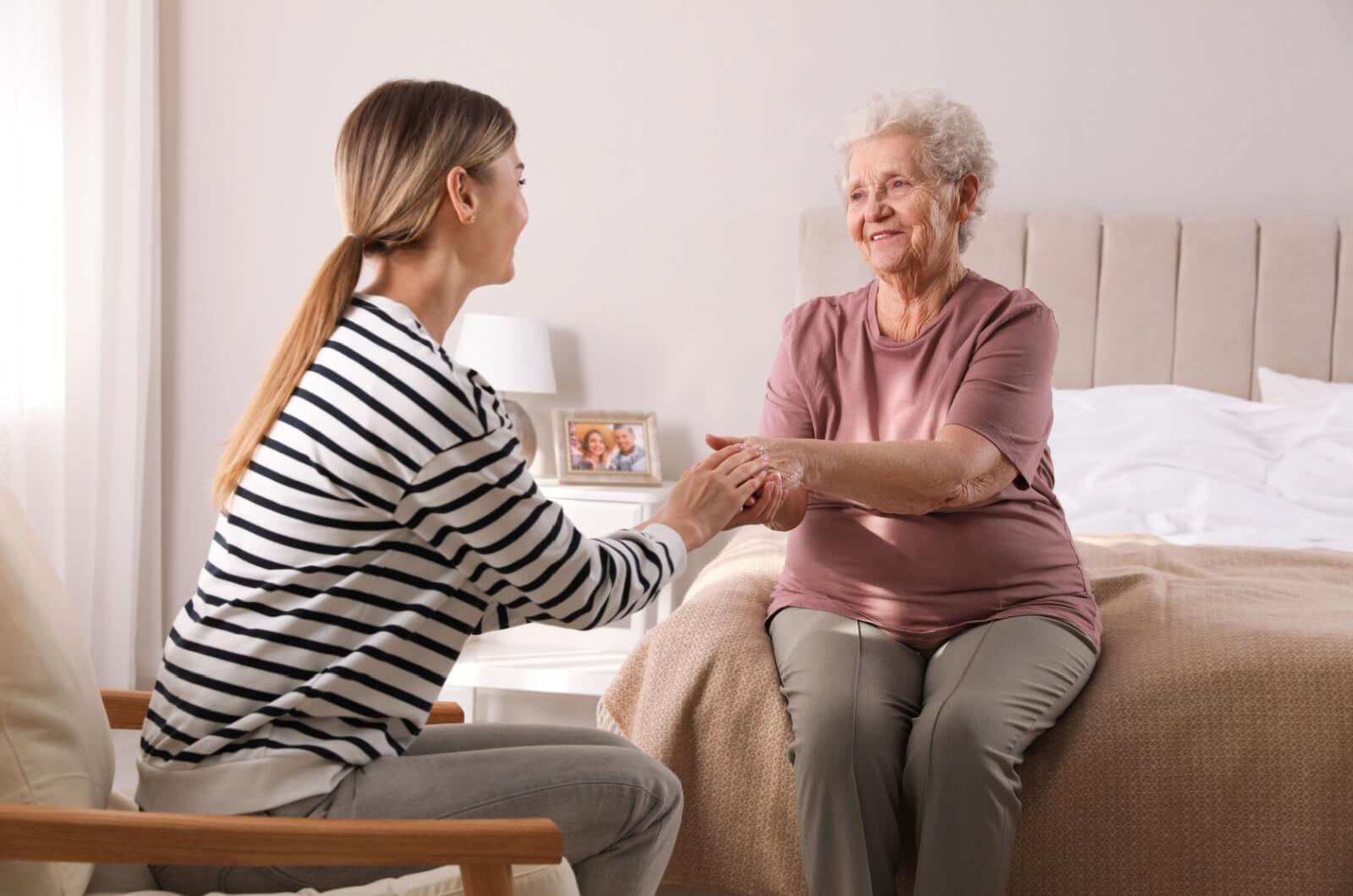 An adult child and a parent with dementia sitting across from each other holding hands during a conversation.