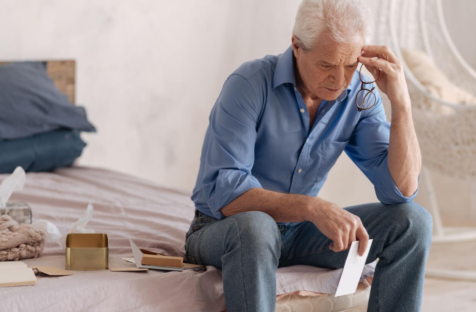 An older adult holding a photograph in their hand while sitting on a bed with memorabilia.