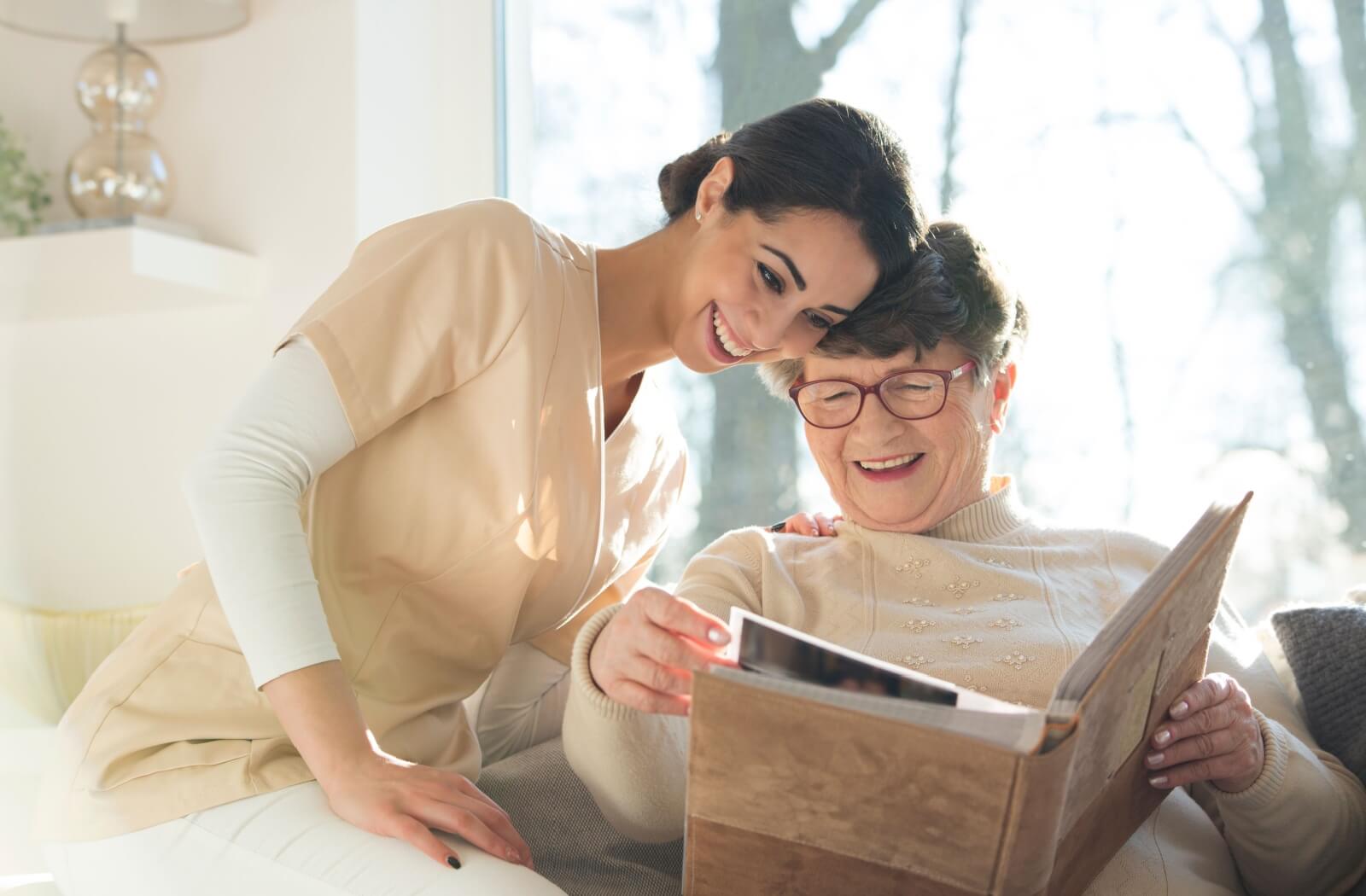 A compassionate memory care caregiver sits with a resident while they look at a photo album.