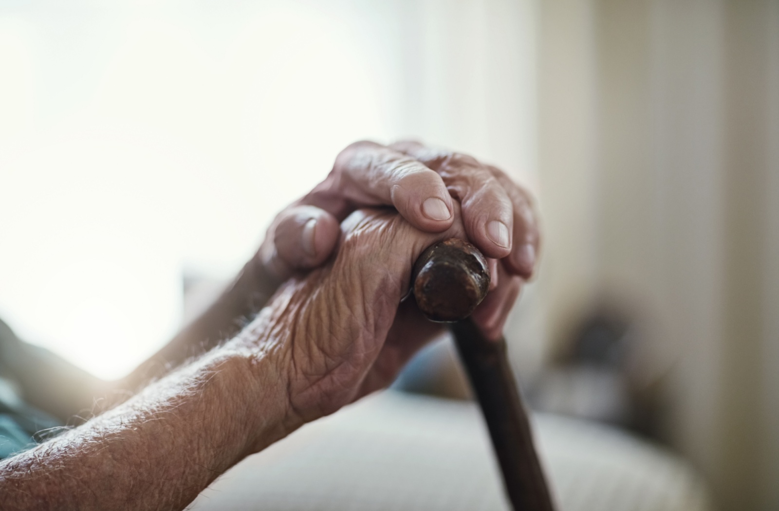 A close-up image of a senior's hands comfortably resting on their cane's handle.