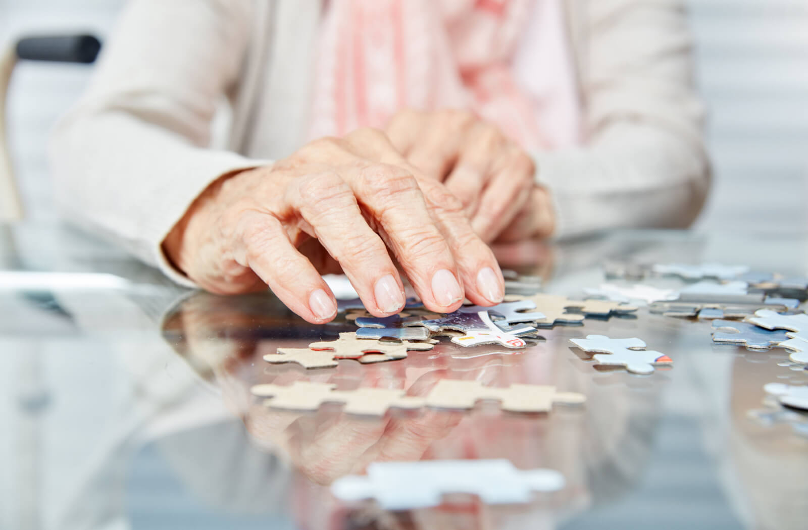 A close-up image of the hand of an older adult with dementia while they assemble a jigsaw puzzle.
