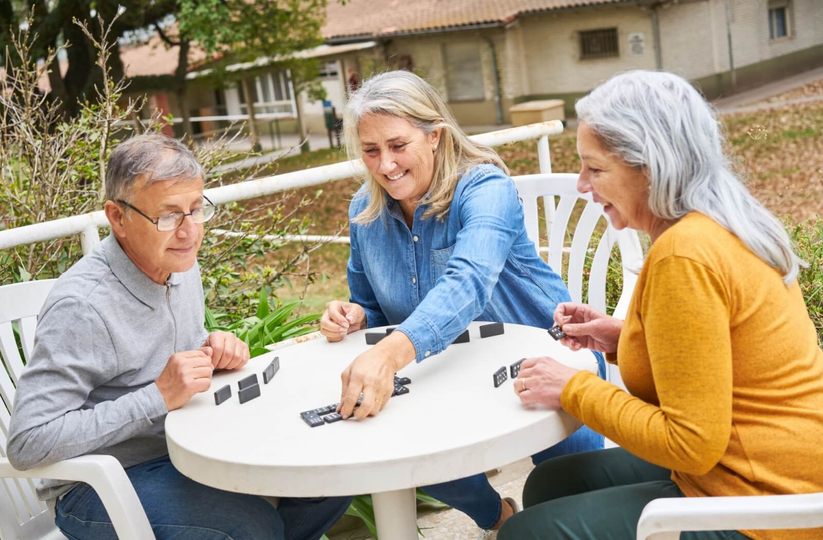 Three seniors with dementia play a game of dominoes together outside during social time at memory care
