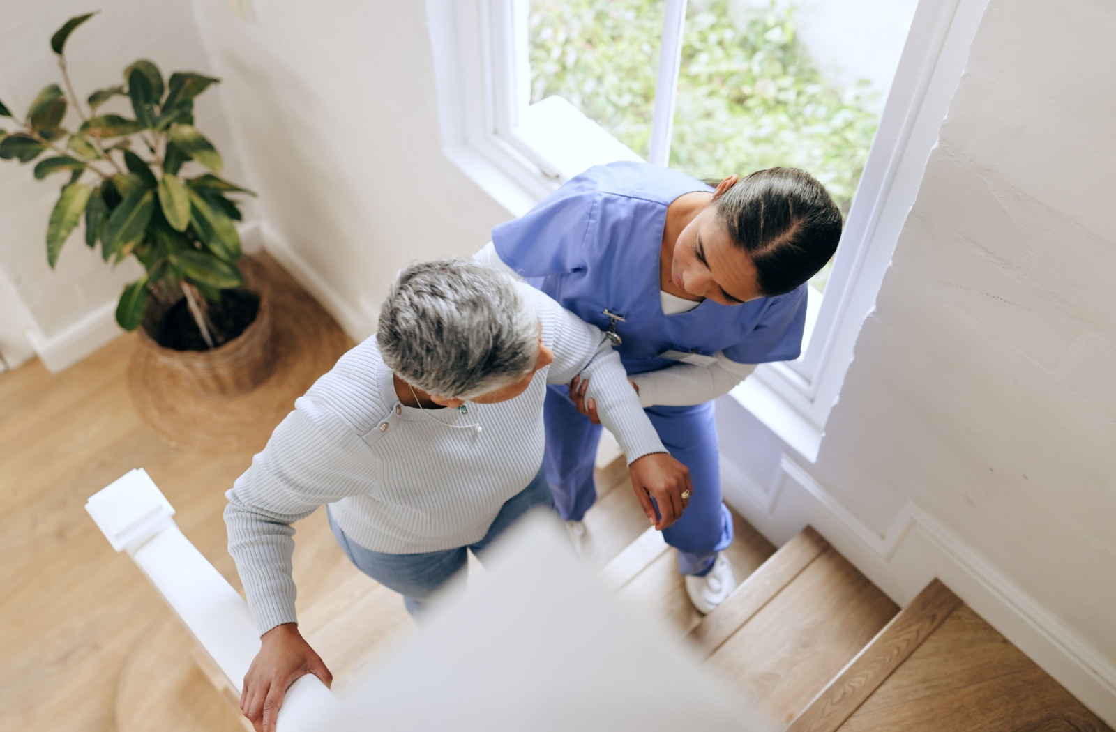 A nurse helps a senior with mobility needs up the stairs to help prevent unnecessary falls
