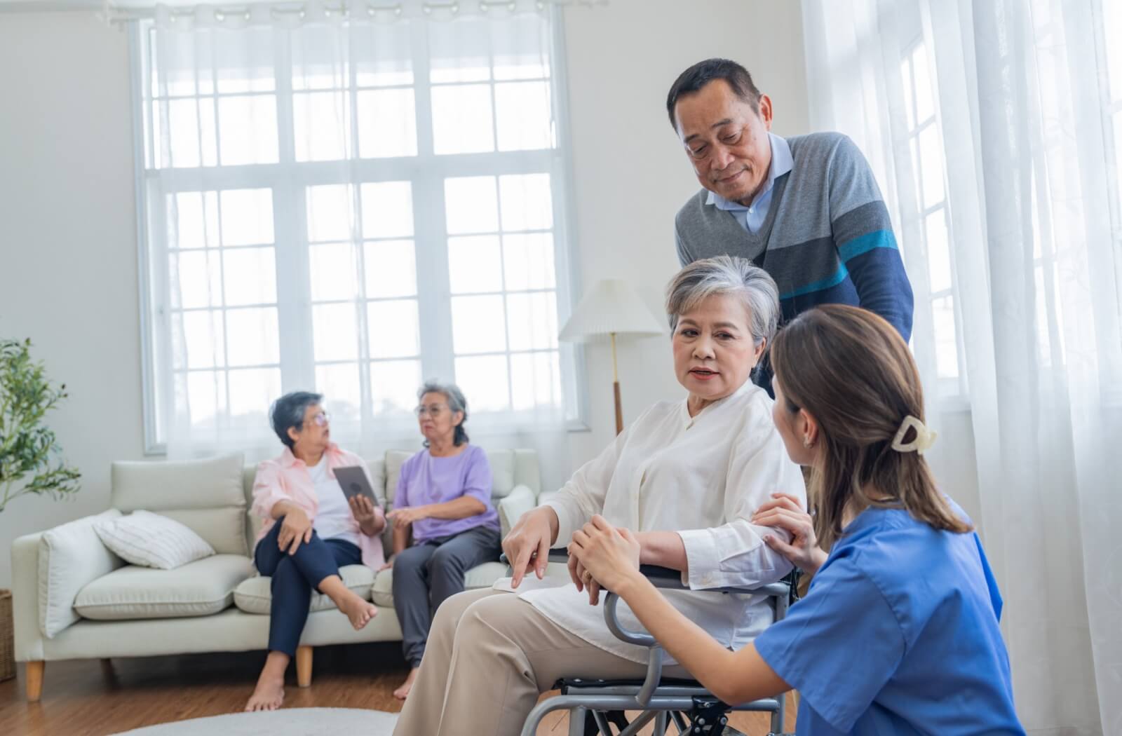 A nurse checks in on a senior couple hanging out in a communal space in their assisted living community